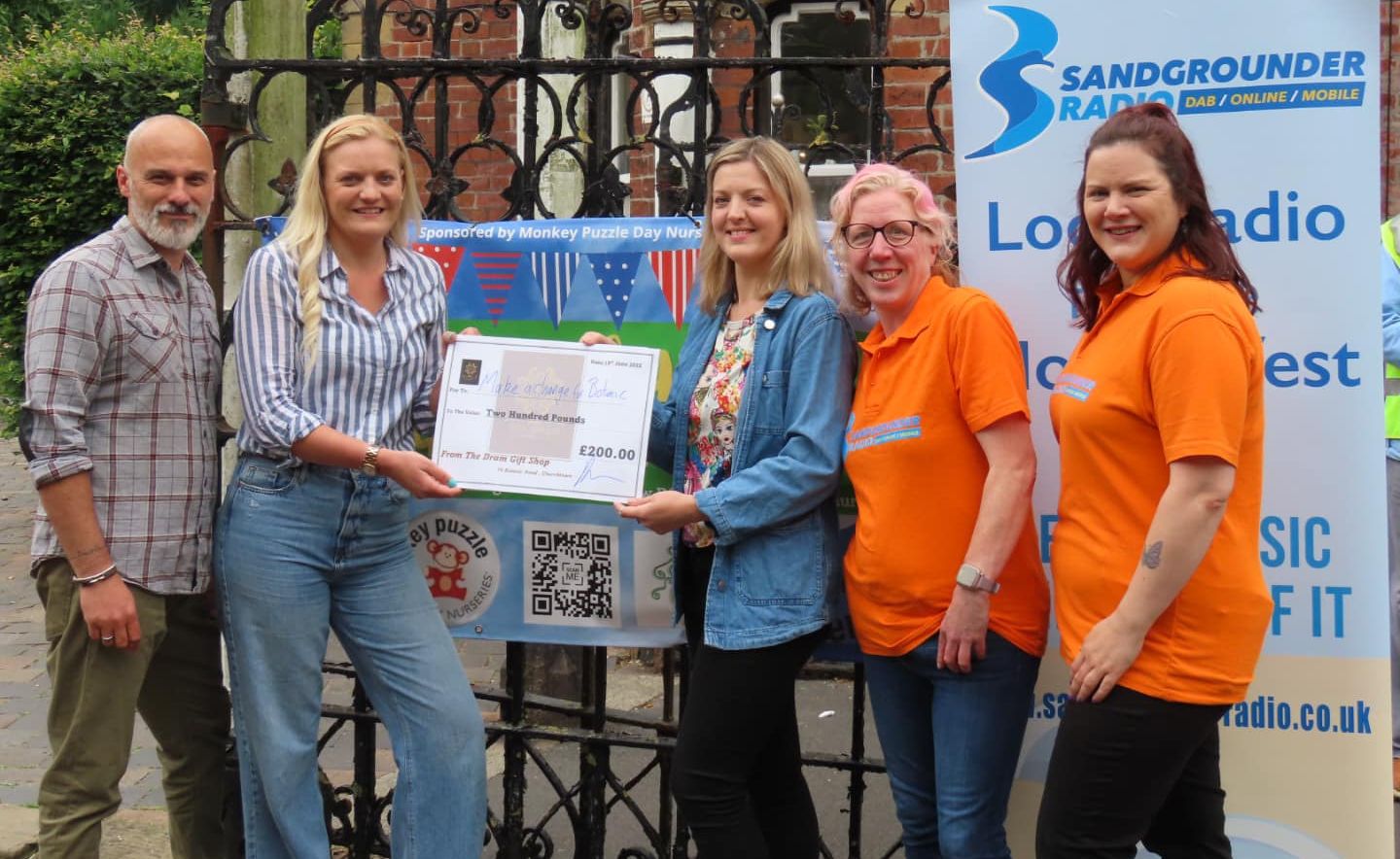 Owner of The Dram Gift Shop Darren Boyd-Preece (left), competition winner Ruth Peacock (third left) and representatives from Sandgrounder Radio present the £200 cheque to Jess thwaites (second left) from Make A Change For Botanic. Photo by Andrew Brown Media