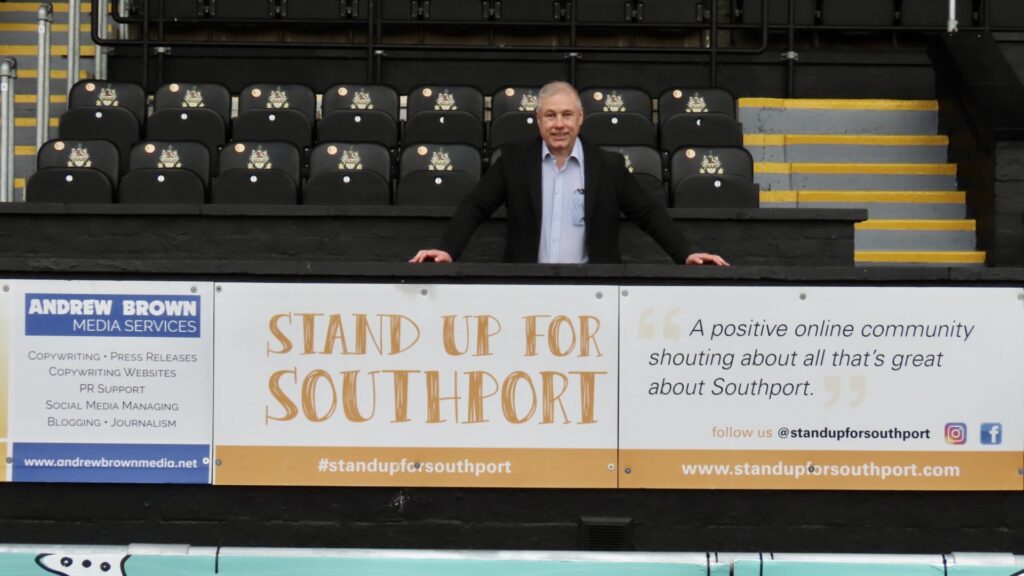 Stand Up For Southport founder Andrew Brown with the advertising board at Southport FC