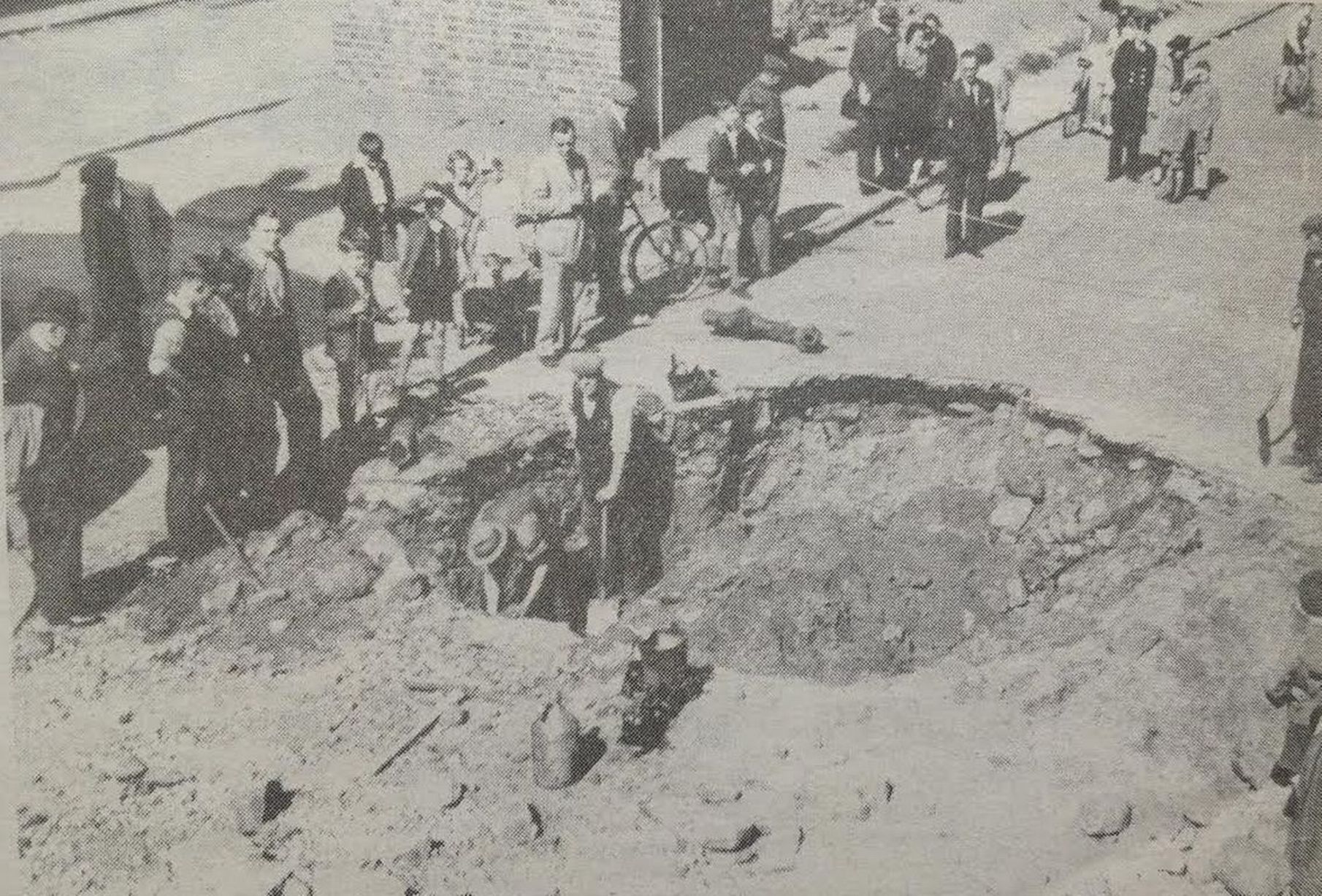Passers-by watch workmen repair a burst water main in this huge bomb crater in East Street in Waterloo after a German bombing raid in 1940 during World War II