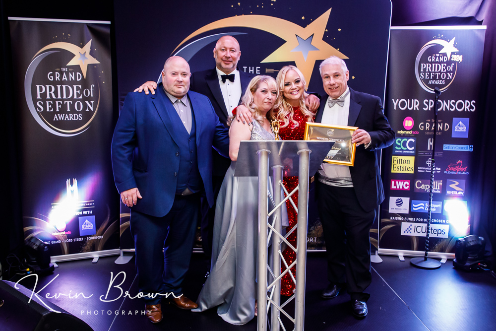 Denise and Stuart Fergus are presented with the Main Award at the 2024 Grand Pride Of Sefton Awards. They are with Mikhail Hotel and Leisure Group Chairman Andrew Mikhail; In demand Radio presenter Claire Simmo; and Stand Up For Southport Diector Andrew Brown. Photo by Kevin Brown Photography