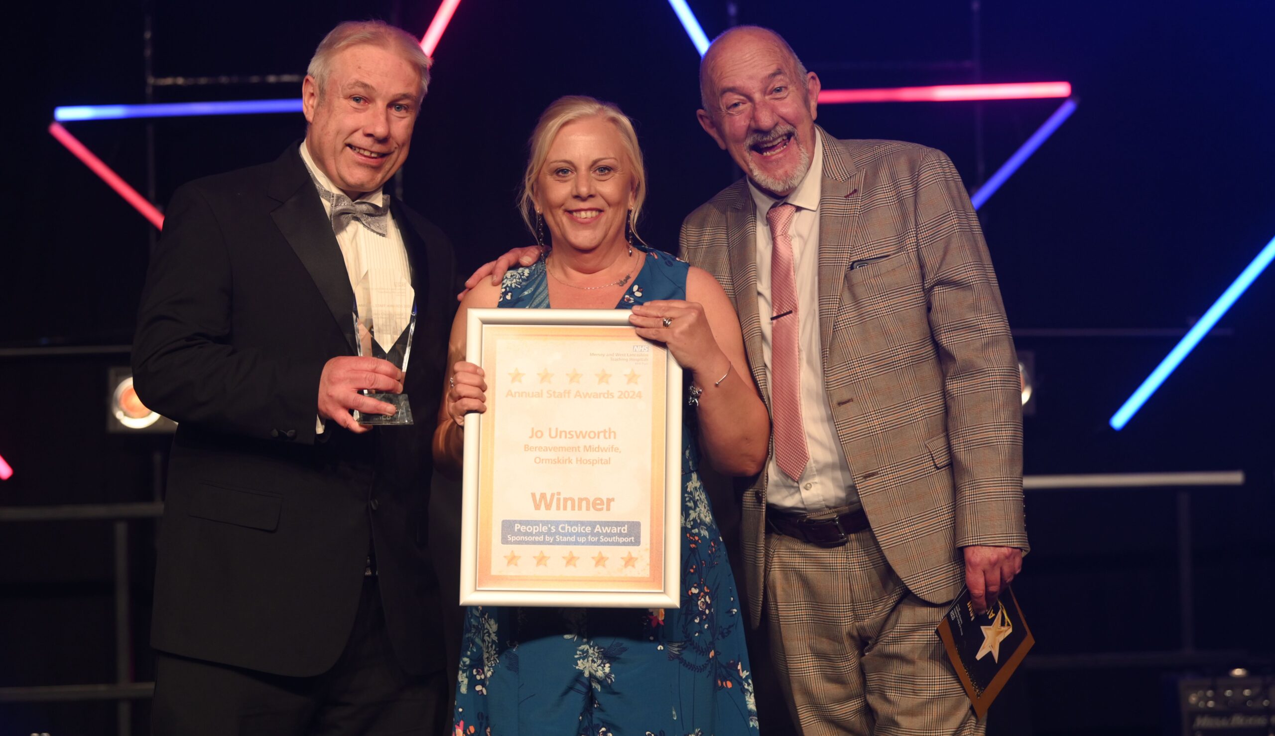 Ormskirk Hospital Specialist Bereavement Midwife Jo Unsworth is awarded the 2024 Stand Up For Southport People’s Choice Award at the first Mersey and West Lancashire Teaching Hospitals NHS Trust staff awards at Liverpool’s M&S Bank Arena by ITV Granada News Reporter Paul Crone and Stand up For Southport Director Andrew Brown