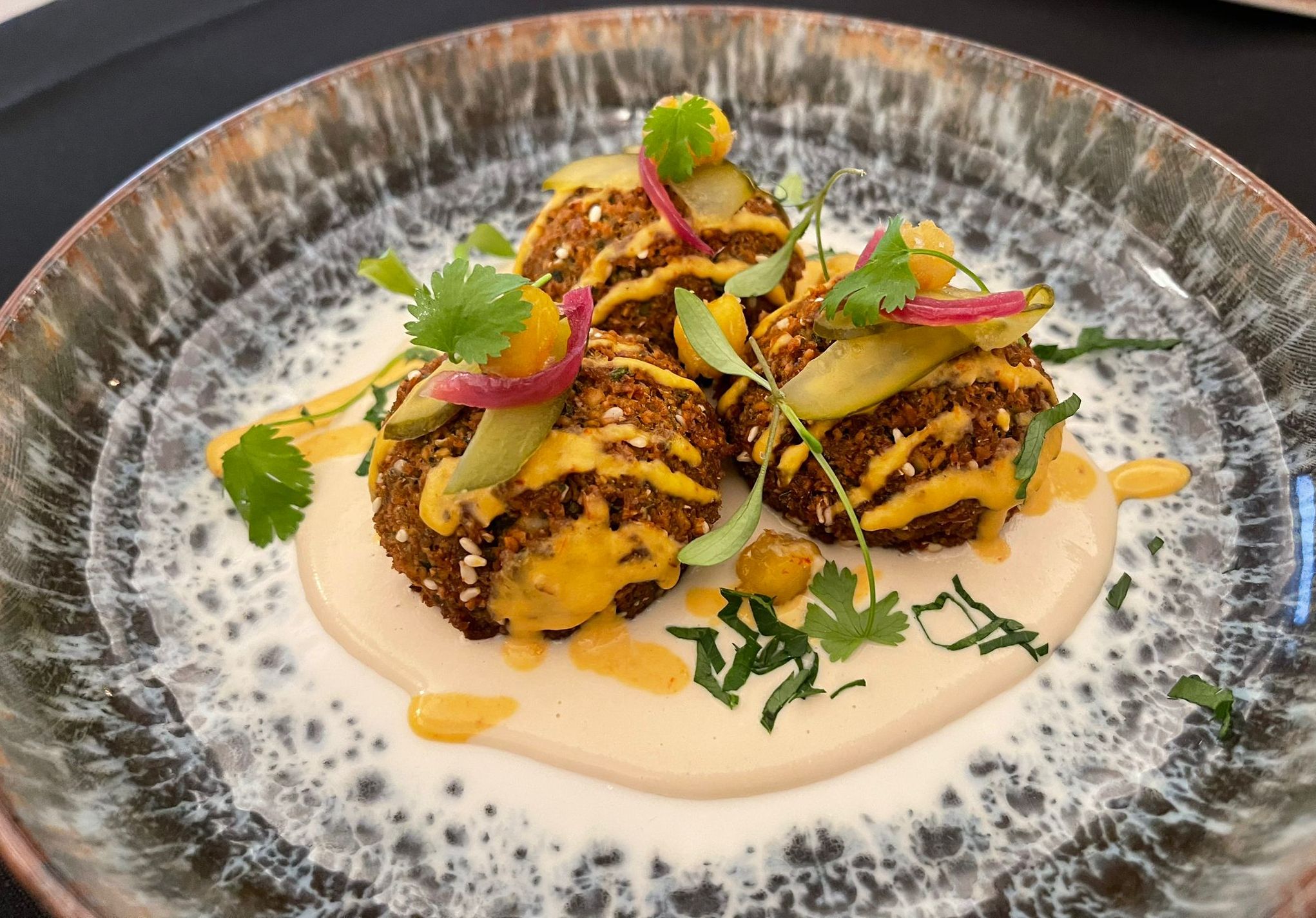 Chickpea and coriander falafel with a tahini sauce on the bottom with a drizzle of a spicy tahini on top at Harry's rooftop bar and terrace at The Grand Southport